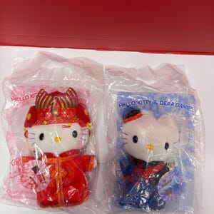 May include: Two Hello Kitty plush toys in plastic packaging. One is dressed in a red Chinese wedding outfit, the other in a blue outfit. The packaging reads "Hello Kitty & Dear Daniel!"