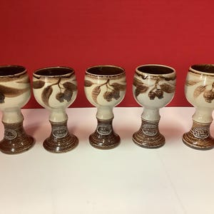 May include: Set of five brown and white ceramic goblets with a floral design. Each goblet has a brown rim and a brown base.