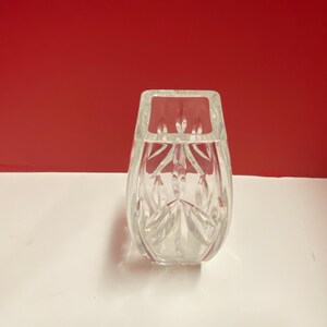 May include: A clear glass vase with a square base and a cut-glass design. The vase is empty and has a reflective surface.