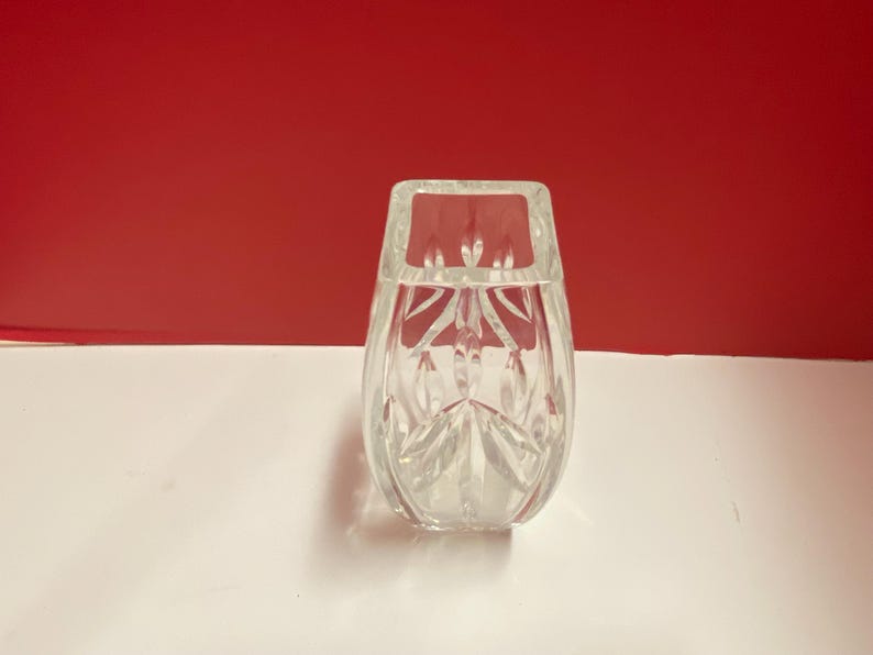 May include: A clear glass vase with a square base and a cut-glass design. The vase is empty and has a reflective surface.