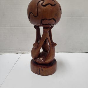 Puede incluir: Escultura de madera de un globo terráqueo sostenido por dos delfines. El globo tiene continentes tallados. Los delfines están colocados con sus colas tocando la base. La escultura está hecha de madera de color marrón oscuro.