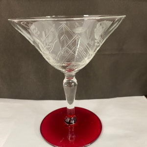 May include: A clear glass martini glass with an etched design and a red base. The glass is on a white surface.