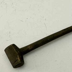 May include: A close-up of a small, dark gray metal hammer with a long handle. The hammer is lying on a white surface.