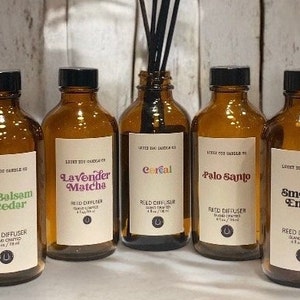 May include: Five amber glass bottles with black lids and white labels. The labels feature different scents: Fir Balsam & Cedar, Lavender Matcha, Cereal, Palo Santo, and Smoke & Ember. Each bottle has a reed diffuser label and a small horseshoe logo.