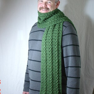 May include: A man wearing a blue baseball cap with the text "Green Bay" on it, a green knitted scarf with tassels, and a gray striped long-sleeved shirt.