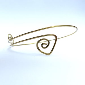 May include: A gold wire bracelet with a spiral design. The bracelet is made of thin wire and has a delicate look.