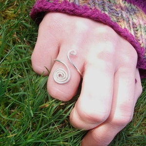 May include: A silver wire ring with a spiral design. The ring is worn on a finger.