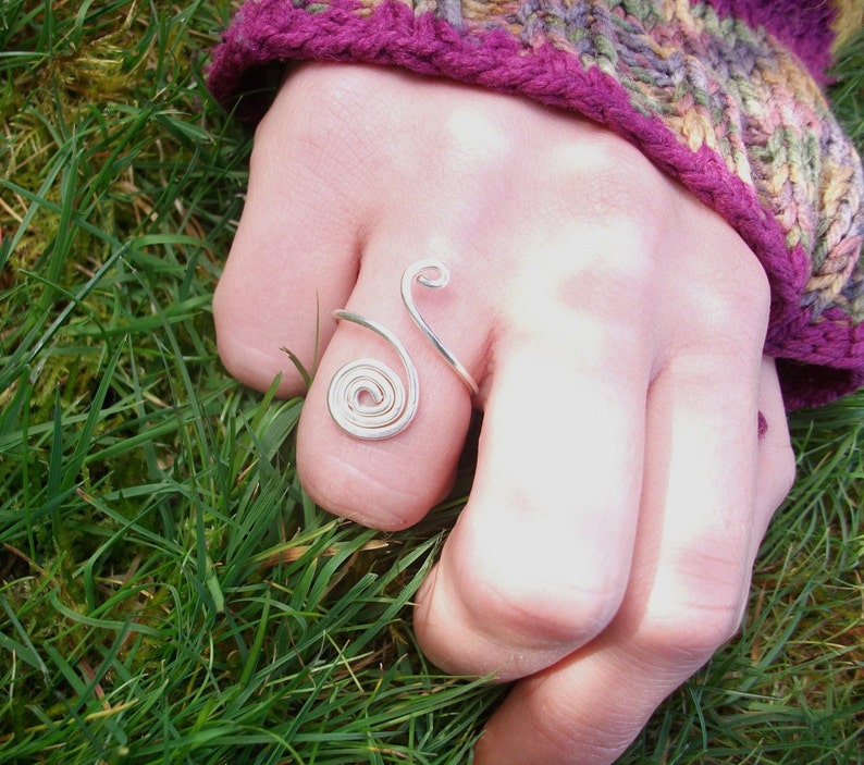 May include: A silver wire ring with a spiral design. The ring is worn on a finger.