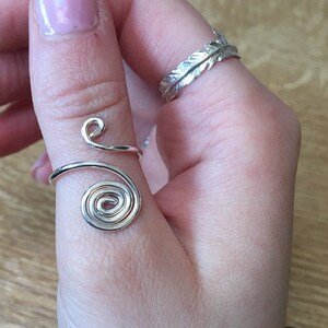 May include: A silver thumb ring with a spiral design. The ring is made of wire and is wrapped around the thumb.