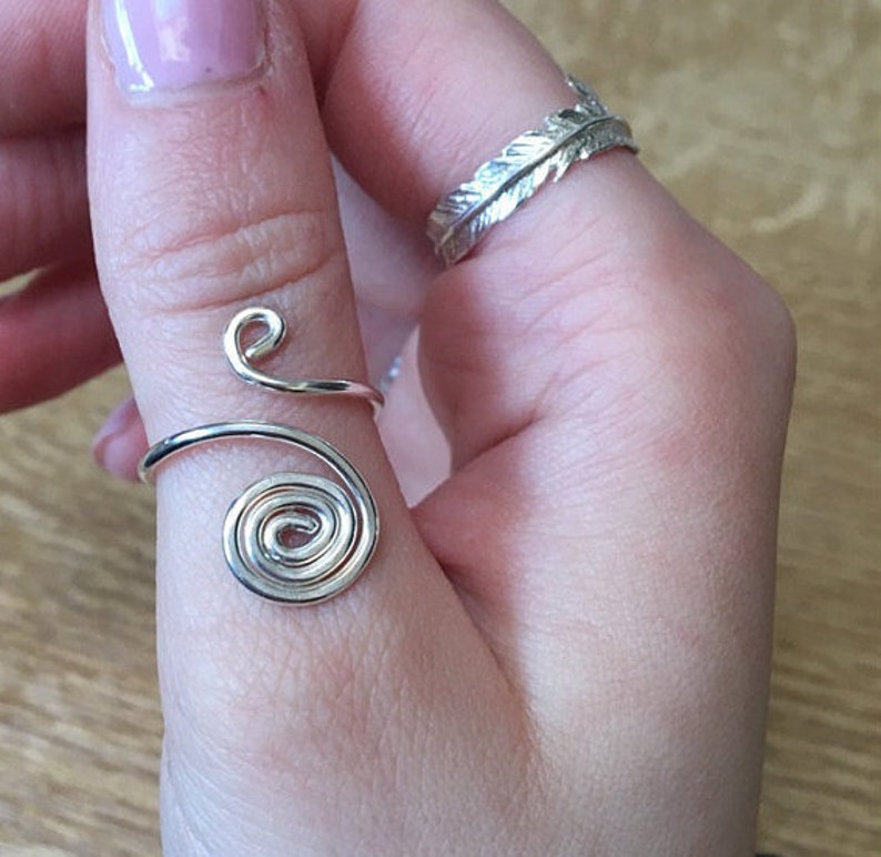 May include: A silver thumb ring with a spiral design. The ring is made of wire and is wrapped around the thumb.
