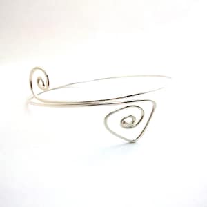 以下が含まれることがあります： 螺旋模様のシルバーワイヤーブレスレット。ブレスレットはオープンタイプで、シンプルでエレガントな外観です。