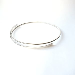 May include: A silver double-wrap bangle bracelet with a simple, minimalist design.