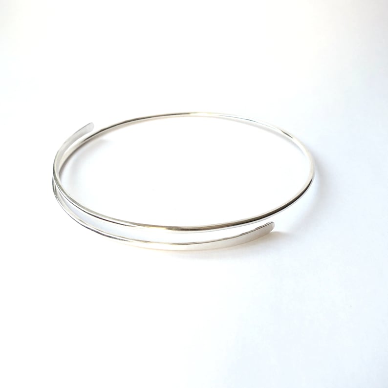 May include: A silver double-wrap bangle bracelet with a simple, minimalist design.