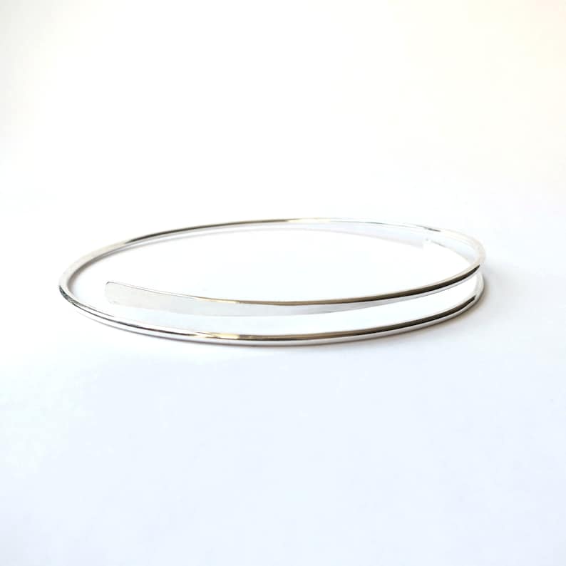 May include: A silver double-wrap bangle bracelet. The bracelet is made of two thin bands of metal that are wrapped around the wrist.