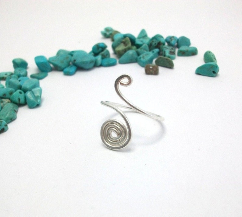 May include: A silver wire ring with a spiral design. The ring is open and adjustable.