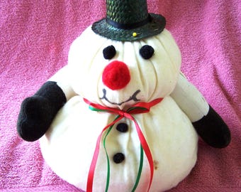 Könnte beinhalten: Ein weißer Schneemann mit einem schwarzen Hut, einer roten Nase und schwarzen Knöpfen. Der Schneemann trägt ein grünes und rotes Band um den Hals und sitzt auf einem rosa Handtuch.
