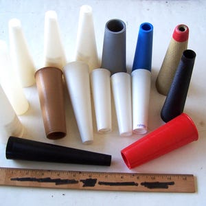 May include: A collection of various colored yarn cones, including white, brown, gray, blue, black, red, and tan. A wooden ruler with inch markings is at the bottom of the image.