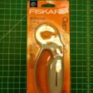 May include: A Fiskars Classic Rotary Cutter with an orange handle and a silver blade. The cutter is packaged in a clear plastic blister pack with a white and orange background.
