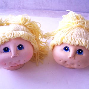 Puede incluir: Dos cabezas de muñeca hechas a mano con pelo de lana. Las muñecas tienen ojos azules y mejillas sonrosadas.