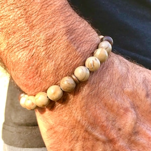 May include: A brown and beige beaded bracelet with a silver accent. The bracelet is made of natural materials and has a rustic look.