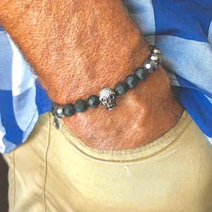 May include: A black onyx bracelet with a silver skull charm. The skull has small clear stones for eyes.