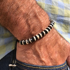 May include: A black and white beaded bracelet with a black cord and a toggle clasp. The bracelet is made of round beads with alternating black and white stripes.