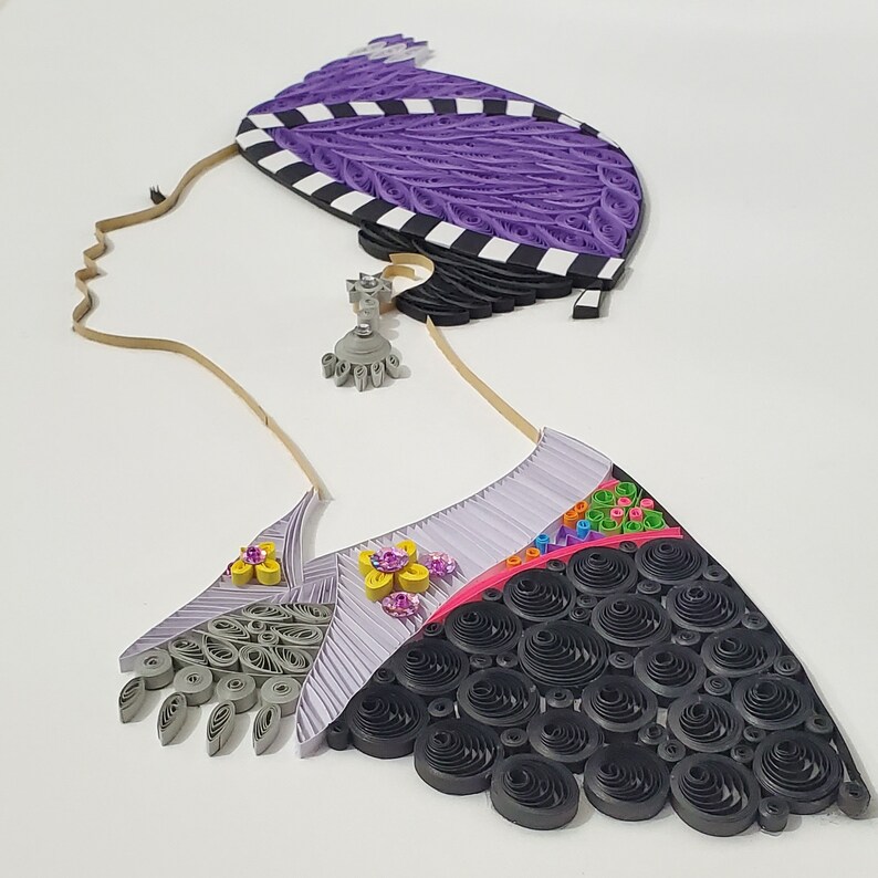 May include: A paper craft depicting a woman's head with a detailed, intricate design. The woman is wearing a black and white patterned head covering and a black and white patterned dress with a purple, pink, and yellow floral design.