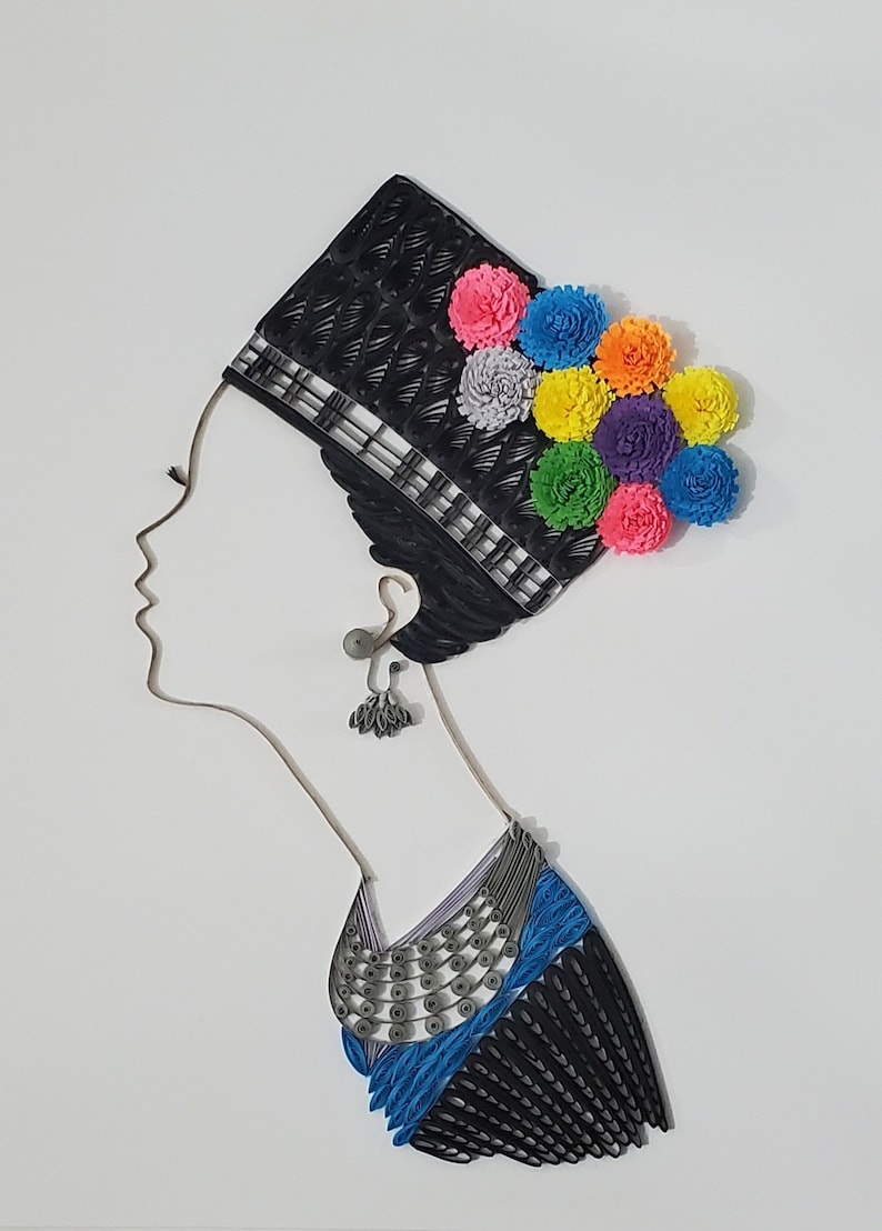 Op de afbeelding: Een kunstwerk van papierquilling dat het profiel van een vrouw toont die een zwarte hoed draagt met een kleurrijk bloemenontwerp en een blauwe en zilveren ketting.