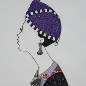 May include: A paper quilling artwork depicting a woman wearing a purple and white patterned head covering, a silver earring, and a black and white patterned shirt with floral accents.