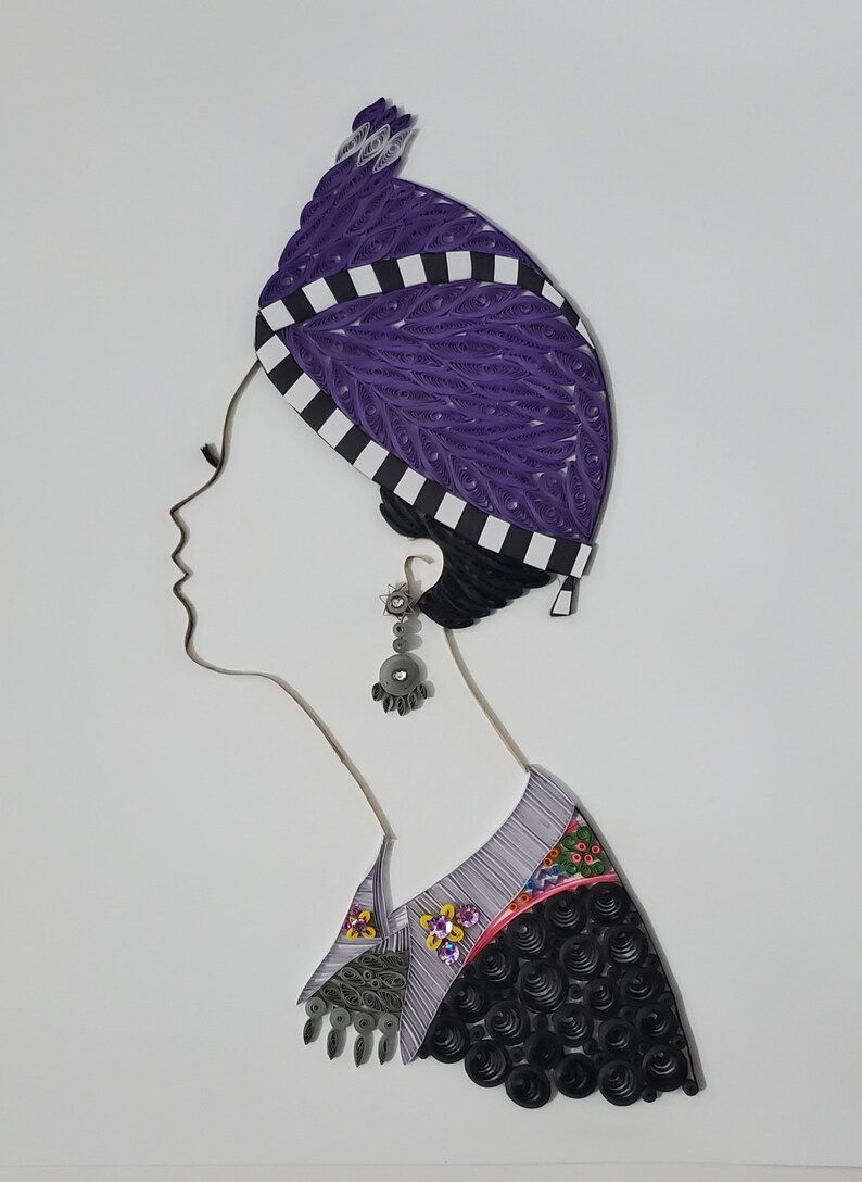 May include: A paper quilling artwork depicting a woman wearing a purple and white patterned head covering, a silver earring, and a black and white patterned shirt with floral accents.