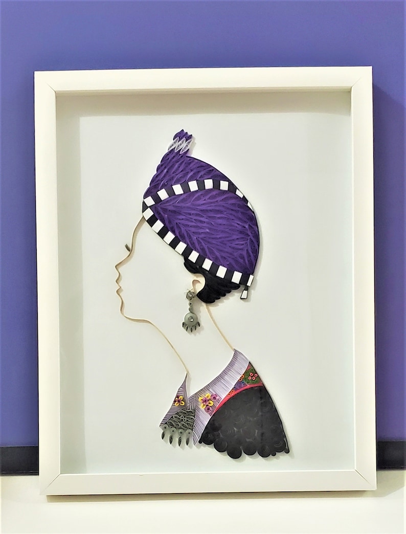 May include: A framed paper art piece depicting a woman's profile wearing a purple and white patterned head covering and a black and white patterned garment. The artwork is created using the quilling technique.