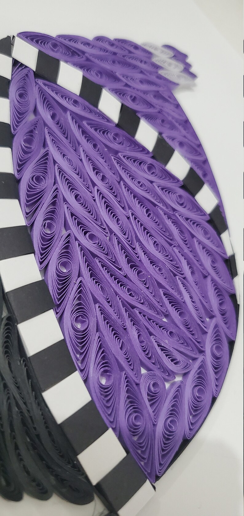 May include: Purple and black paper craft art with a geometric pattern. The purple section is made of rolled paper and the black and white section is made of stripes.