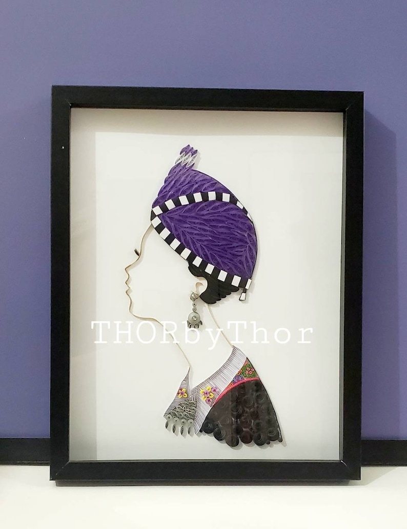May include: A framed paper art piece depicting a woman's profile wearing a purple and white patterned head covering. The woman is wearing a black and white patterned shirt with a floral design. The artwork is signed "THORbyThor".