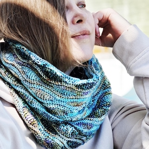 Puede incluir: Una bufanda infinita de punto grueso con una paleta de colores variados en turquesa brillante, azul marino profundo y toques de verde bosque. El hilo texturizado crea un patrón ondulado y giratorio en todo el diseño circular del cuello.