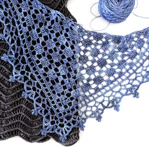 Puede incluir: Primer plano de tres chales de ganchillo en tonos azules y grises. Los chales presentan intrincados patrones calados y bordes decorativos. Una madeja de hilo azul se encuentra en la esquina superior derecha, lo que sugiere un proyecto artesanal.