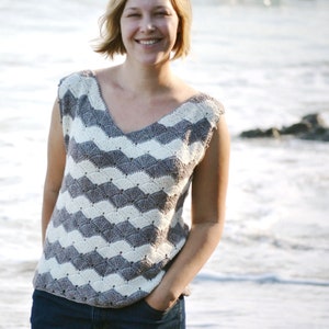 Könnte beinhalten: Ein ärmelloses Häkeltop mit einem Chevron-Muster in Weiß und Grau. Das Oberteil hat einen V-Ausschnitt und wird von einer Person getragen, die an einem Strand steht.