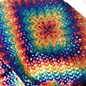 May include: A colorful crocheted blanket with a rainbow pattern. The blanket is made with a variety of yarn colors, including red, orange, yellow, green, blue, indigo, and violet.