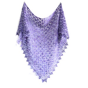 Puede incluir: Un chal hecho a mano, de tejido abierto, en tonos morado, lavanda y blanco. El chal triangular presenta un delicado patr&oacute;n de encaje y un borde festoneado. El chal se muestra sobre un fondo blanco, destacando su intrincado dise&ntilde;o.