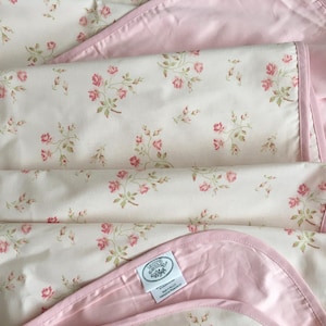 May include: A pink and white floral patterned baby blanket with a pink satin trim. The blanket has a small tag with the text "Southern Hospitality" on it.