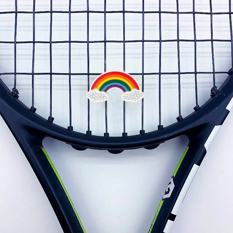 May include: A rainbow-colored tennis racket charm with white clouds. The charm is attached to a black tennis racket.
