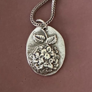 Peut inclure: Un collier avec un pendentif en argent représentant une fleur d'hortensia avec des feuilles en relief.
