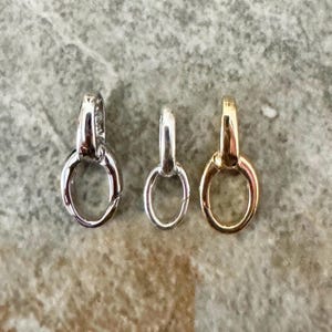 May include: Three oval-shaped jewelry connectors arranged in a row. The left connector is silver-toned, the middle connector is a smaller silver-toned version, and the right connector is gold-toned. Each piece features a hinged mechanism for opening.