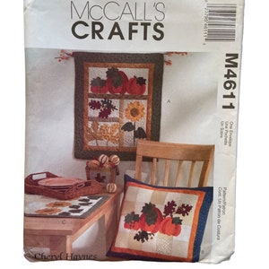 May include: A McCall's Crafts sewing pattern for a fall-themed quilt. The pattern includes instructions for making a pillow and a wall hanging with pumpkins, leaves, and sunflowers. The pattern is titled "M4611".