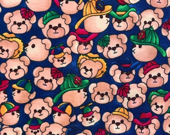 以下が含まれることがあります： さまざまな帽子をかぶったピンクのぬいぐるみが繰り返し描かれた青い布。帽子は、カウボーイハット、ベースボールキャップ、ボンネットなど、さまざまな色とスタイルがあります。