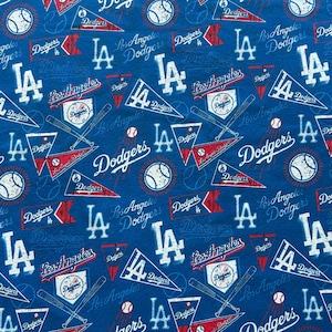 Puede incluir: Una tela azul con un patrón repetitivo de logotipos de béisbol de los Los Angeles Dodgers, banderines, pelotas de béisbol y bates cruzados. El diseño incluye el texto Dodgers y Los Angeles Dodgers en blanco y rojo, con el monograma LA en blanco.