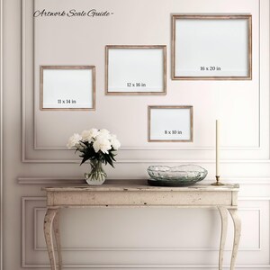 a gallery wall with three framed artworks of different sizes, and a small table with a vase of white flowers in front of it.