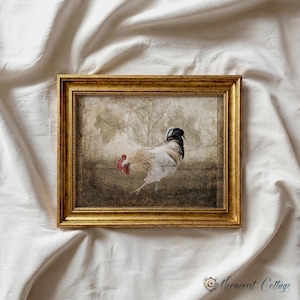 a rooster standing in a field, framed in a gold frame and displayed on a white cloth.