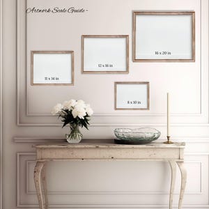a gallery wall with three framed artworks of different sizes, and a small table with a vase of white flowers in front of it.