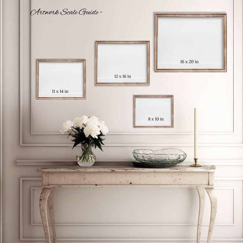 a gallery wall with three framed artworks of different sizes, and a small table with a vase of white flowers in front of it.