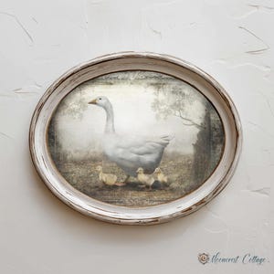 A white oval frame with a painting of a mother goose and her three ducklings on a grassy field.